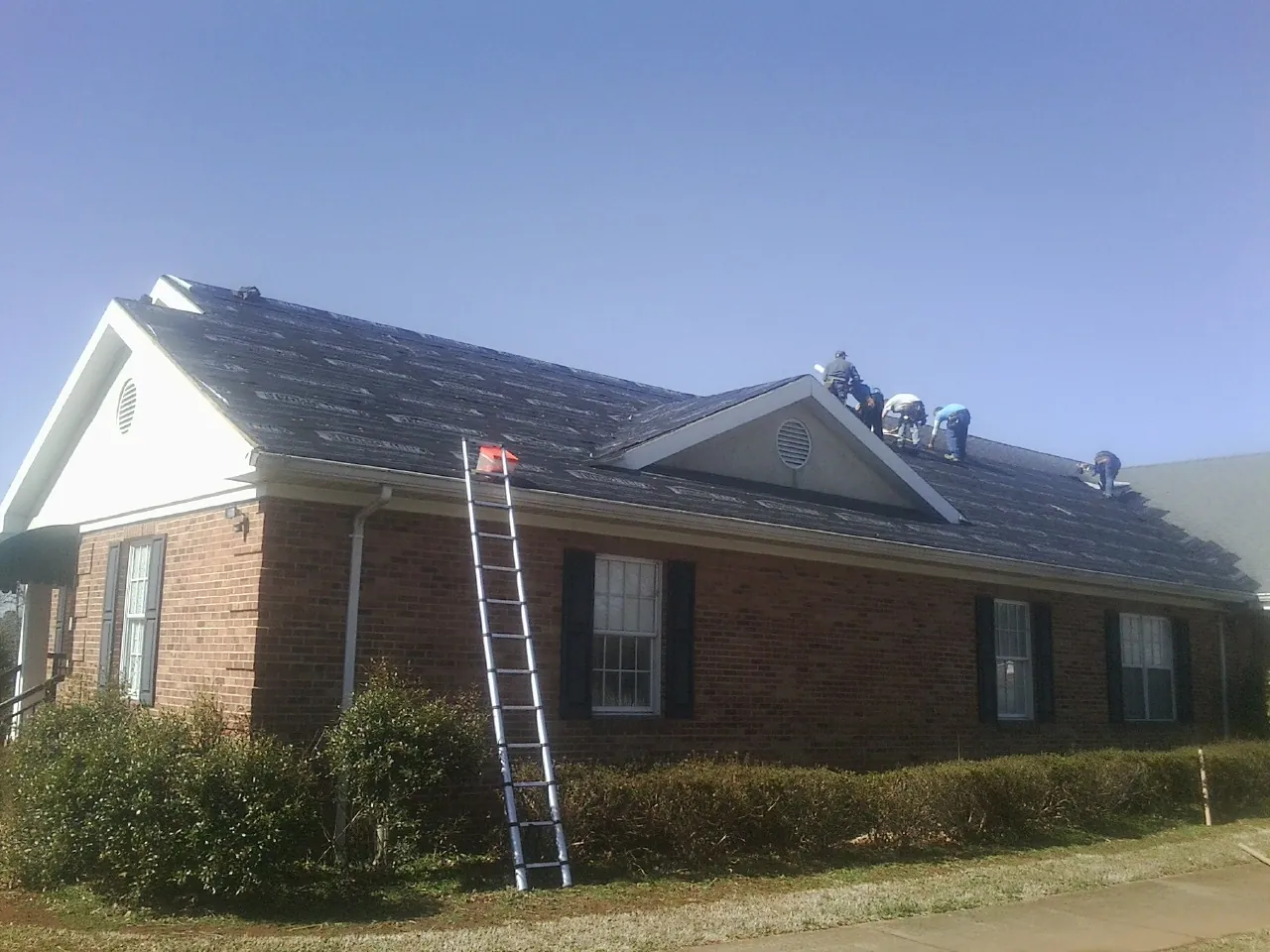 Crew tearing shingles off a brick ranch roof with a ladder set — Metal Roof Repair work by our crew in Chapel Hill