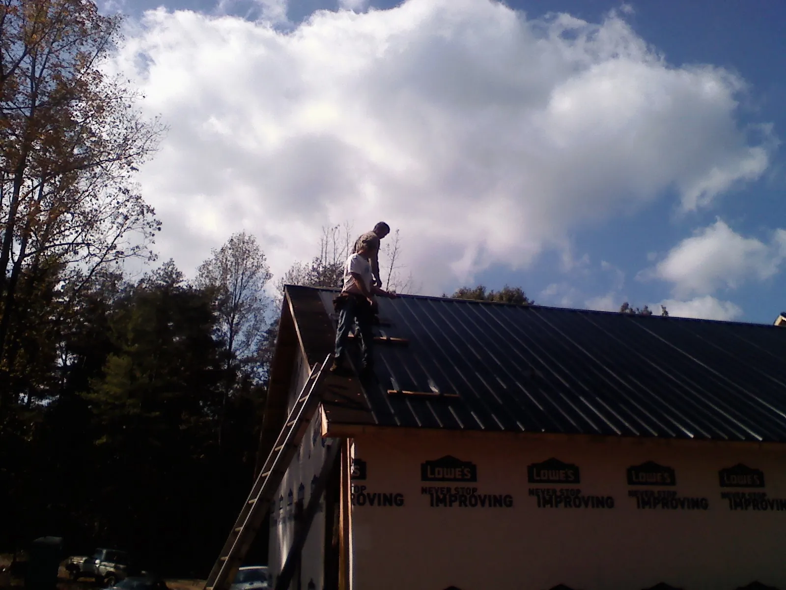 Roofer fastening dark metal panels high against a cloudy sky, from a Roof Inspection job in Chapel Hill